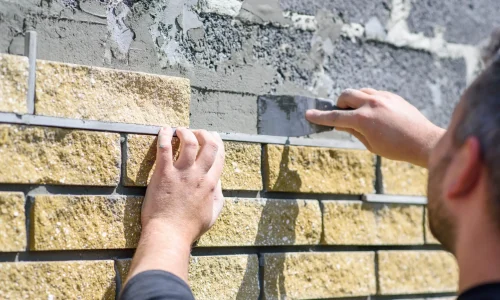 Installer applying stone cladding to the exterior wall of a house for a natural, durable finish — by Cladding Wellington. Installer applying stone cladding to the exterior wall of a house for a natural, durable finish — by Cladding Wellington.